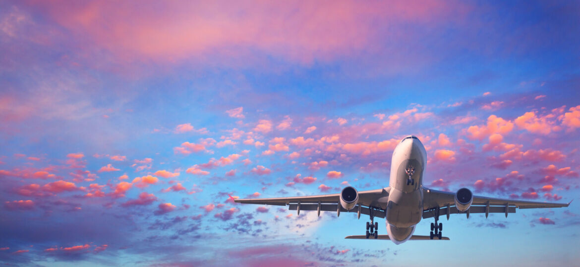 Passenger airplane is flying in the blue sky with pink clouds